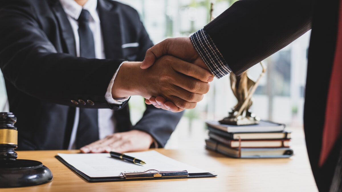 Two business people in suits shaking hands above a signed agreement.