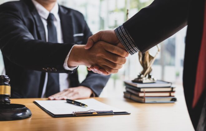 Two business people in suits shaking hands above a signed agreement.