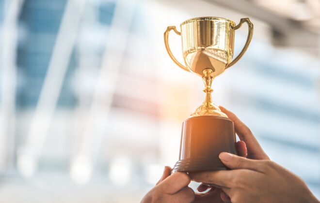 A golden trophy behind held in the air by two hands.