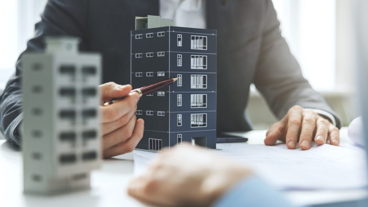 A man uses a pen to point at a commercial real estate property while sitting across the desk from a client.