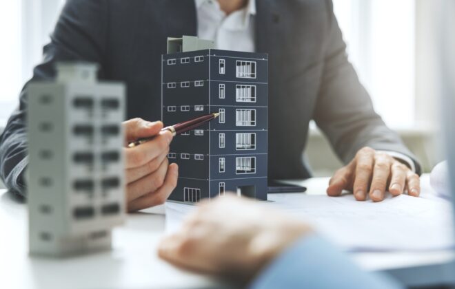 A man uses a pen to point at a commercial real estate property while sitting across the desk from a client.